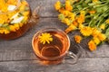 Cup of herbal tea and transparent teapot and marigold flowers on wood background. Calendula Tea Benefits Your Health Royalty Free Stock Photo