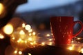 Cup of hot beverage on balcony railing decorated with Christmas lights, space for text
