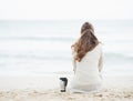 Cup of hot beverage near woman in sweater sitting on lonely beach Royalty Free Stock Photo