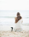 Cup of hot beverage near young woman in sweater sitting on beach Royalty Free Stock Photo