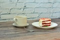 A cup of hot black coffee on a saucer, a fork and a plate with a piece of red velvet cake on a wooden table Royalty Free Stock Photo