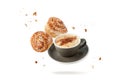 Cup hot cappucino coffee and fresh baked cinnamon buns with crumbs and sugar pieces flying falling isolated on white Royalty Free Stock Photo