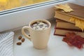 Cup of hot chocolate with almond and books on the windowsill. Window in a background. Fall time. Autumn composition. Home comfort