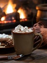 Cup of hot chocolate and marshmallows with fireplace burning in background