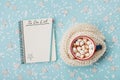 Cup of hot cocoa or chocolate with marshmallow and notebook with to do list on blue confetti background top view. Christmas plan. Royalty Free Stock Photo