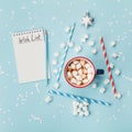 Cup of hot cocoa or chocolate, stylish fir tree and wish list on turquoise confetti background top view. Christmas concept. Royalty Free Stock Photo