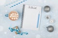 Cup of hot cocoa, gift, holiday decorations and notebook with to do list on blue vintage table from above, christmas planning.