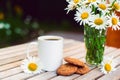 Cup of hot coffee, biscuits and a bouquet of chamomiles.