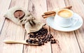 Cup of hot coffee, cinnamon sticks and coffee beans in a wooden scoop and spilling out from a hessian bag on wooden Royalty Free Stock Photo