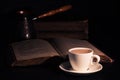 Cup of hot coffee, copper cezve and open Torah page on black wood table in the dark. Closeup Royalty Free Stock Photo