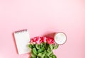 The cup of hot coffee, empty notepad with funny pen and bouquet of fresh roses on soft pink background Royalty Free Stock Photo