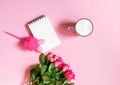 The cup of hot coffee, empty notepad with funny pen and bouquet of fresh roses on soft pink background Royalty Free Stock Photo