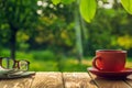 Cup of hot coffee and glasses with a newspaper on a wooden table in a green garden in the morning. Summer background Royalty Free Stock Photo