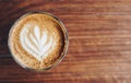 A cup of hot coffee with latte art on the wooden table.