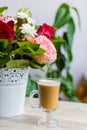 Cup of hot coffee with milk stands near the window and a bright colored bouquet of flowers Royalty Free Stock Photo