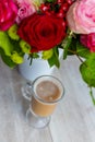 Cup of hot coffee with milk stands near the window and a bright colored bouquet of flowers Royalty Free Stock Photo