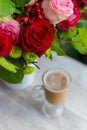 Cup of hot coffee with milk stands near the window and a bright colored bouquet of flowers Royalty Free Stock Photo