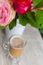 Cup of hot coffee with milk stands near the window and a bright colored bouquet of flowers Royalty Free Stock Photo