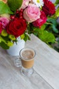 Cup of hot coffee with milk stands near the window and a bright colored bouquet of flowers Royalty Free Stock Photo