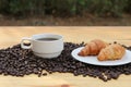 A cup of hot coffee and on roasted beans croissant with bokeh background