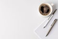 A cup of hot coffee sits in the corner of a bright workspace, alongside two pens and a notepad, inviting creativity and focus on a Royalty Free Stock Photo