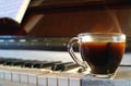 Cup of hot coffee with smoke with blurry piano`s keyboard in background Royalty Free Stock Photo