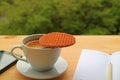 Cup of Hot Coffee with a Stroopwafel Placed on Top with Lined Note Papers and Cellphone on Wooden Table Royalty Free Stock Photo