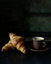 Cup of hot coffee with two fresh croissants against dark background Royalty Free Stock Photo