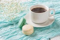 Cup of hot coffee and two macaroons against turquoise fabric background. Sweet breakfast with delicious almond meringue cookies. Royalty Free Stock Photo