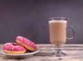 A cup of hot coffee and two tasty pink donuts laying in a white small plate on wooden background Royalty Free Stock Photo