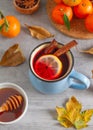 A cup of hot drink with cinnamon, lemon, honey, fruit, spices, autumn leaves on a table