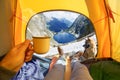 Cup of hot drink in the hand and wonderful mountain lake through the open entrance of the tent. The beauty of a romantic hike and