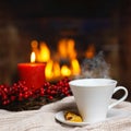 Cup of hot drink with steam and cookie berries red candle in Christmas decoration on knitted plaid in front of fireplace. Royalty Free Stock Photo