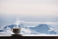 Cup of hot drink with steam on wooden desk and snow capped mountain view in the morning Royalty Free Stock Photo