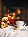 Cup of hot drink teddy bear candle in red Christmas decoration on cozy knitted plaid in front of warm fireplace. Holiday Christmas Royalty Free Stock Photo