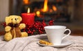 Cup of hot drink teddy bear candle in red Christmas decoration on cozy knitted plaid in front of warm fireplace. Holiday Christmas Royalty Free Stock Photo