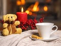 Cup of hot drink teddy bear candle in red Christmas decoration on cozy knitted plaid in front of warm fireplace. Holiday Christmas Royalty Free Stock Photo