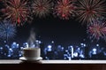 Cup of hot drinks on wooden desk with new year celebrate fireworks, blue defocus Bokeh light of buildings in the city