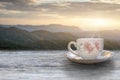 A cup of hot espresso coffee mugs placed with cookies on a wooden floor with morning fog and moutains with sunlight background,