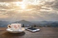 A cup of hot espresso coffee mugs placed with smartphone on a wooden floor with morning fog and moutains with sunlight background,