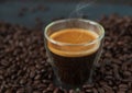 A glass hot espresso coffee with smoke steam over the cup on dark background. Fresh roasted coffee bean background with a cup of Royalty Free Stock Photo