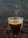 A glass hot espresso coffee with smoke steam over the cup on dark background. Fresh roasted coffee bean background with a cup of Royalty Free Stock Photo