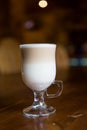 A cup of hot latte coffee in transparent glass on a wooden dark brown table Royalty Free Stock Photo