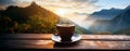 A cup of hot morning coffee with steam on a wooden table against a background of sunrise scene in the mountains.