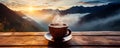 A cup of hot morning coffee with steam on a wooden table against a background of sunrise scene in the mountains.