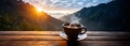 A cup of hot morning coffee with steam on a wooden table against a background of sunrise scene in the mountains. Royalty Free Stock Photo