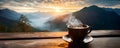 A cup of hot morning coffee with steam on a wooden table against a beautiful background of sunrise scene in the mountains Royalty Free Stock Photo