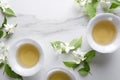 Top view of cups of tasty and healthy green tea, jasmine flowers on the white table.Empty space for text