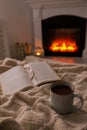 Cup of hot tea, eyeglasses and book near fireplace at home. Cozy atmosphere Royalty Free Stock Photo