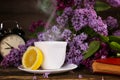 A cup of hot tea with a lemon and over a lilac flowers backdrop